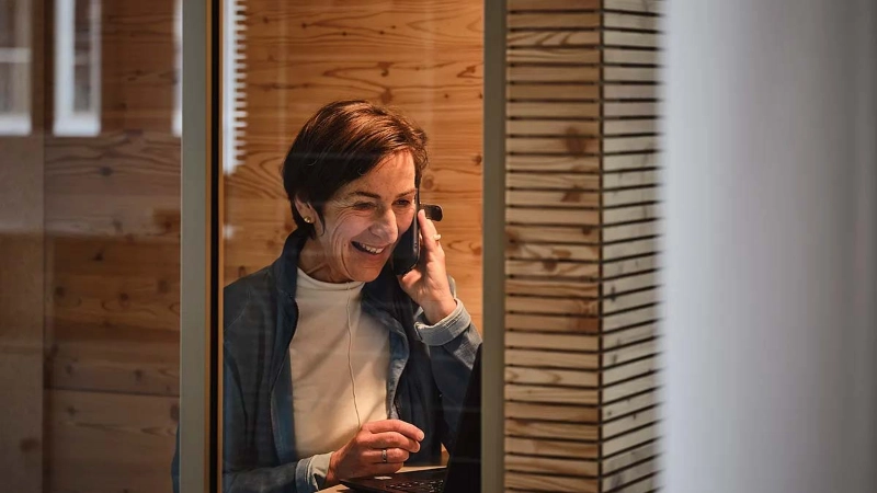 Eine lächelnde ältere Frau sitzt im Büro und telefoniert