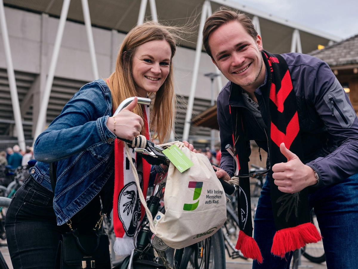 Ein Mann und eine Frau halten eine Goodie Bag am JobRad Aktionsspieltag Klimaschutz und machen beide die Daumen hoch Geste